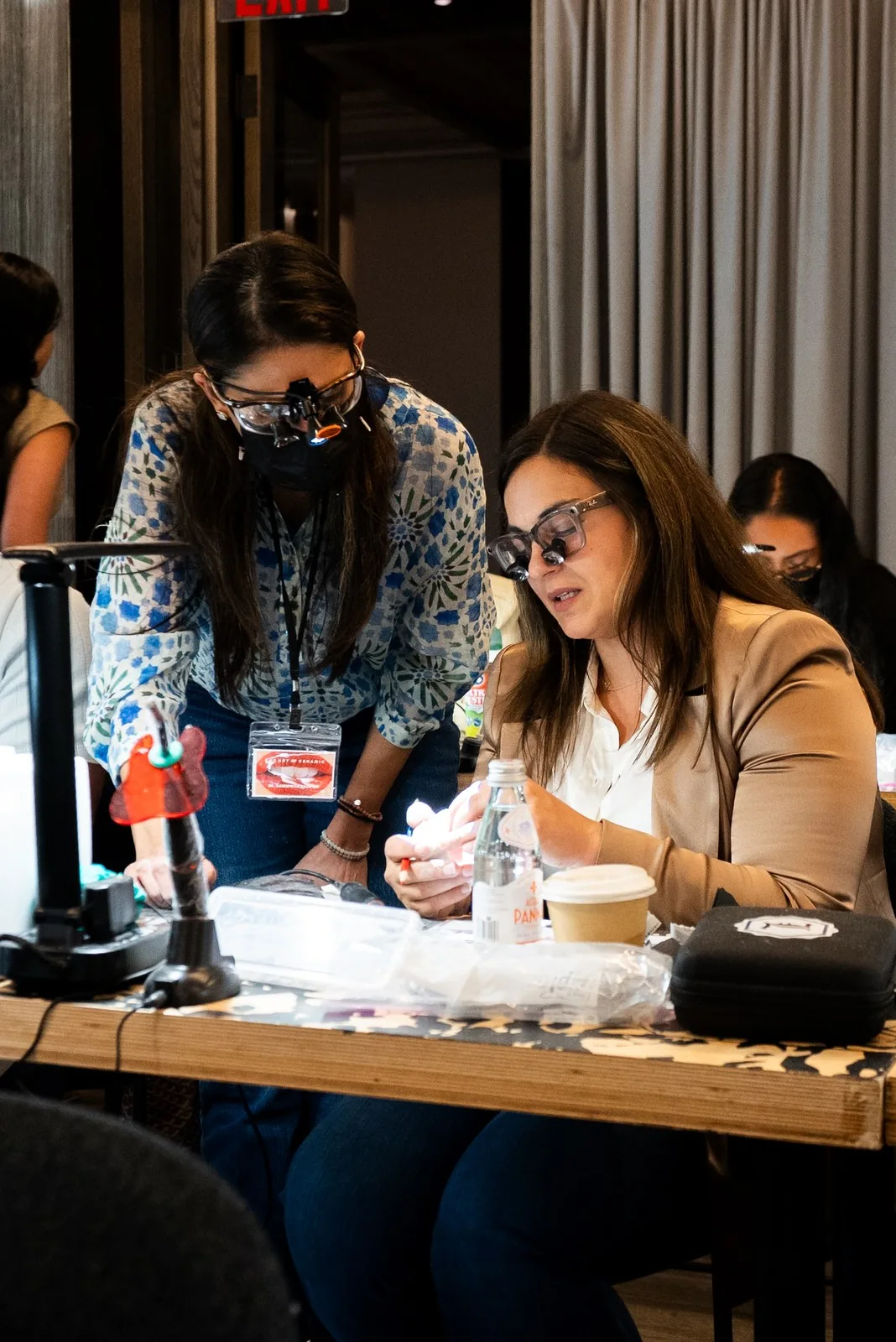 Dr. Andi-Jean Miro, in loupes, works material at a bench while a dentist leans in