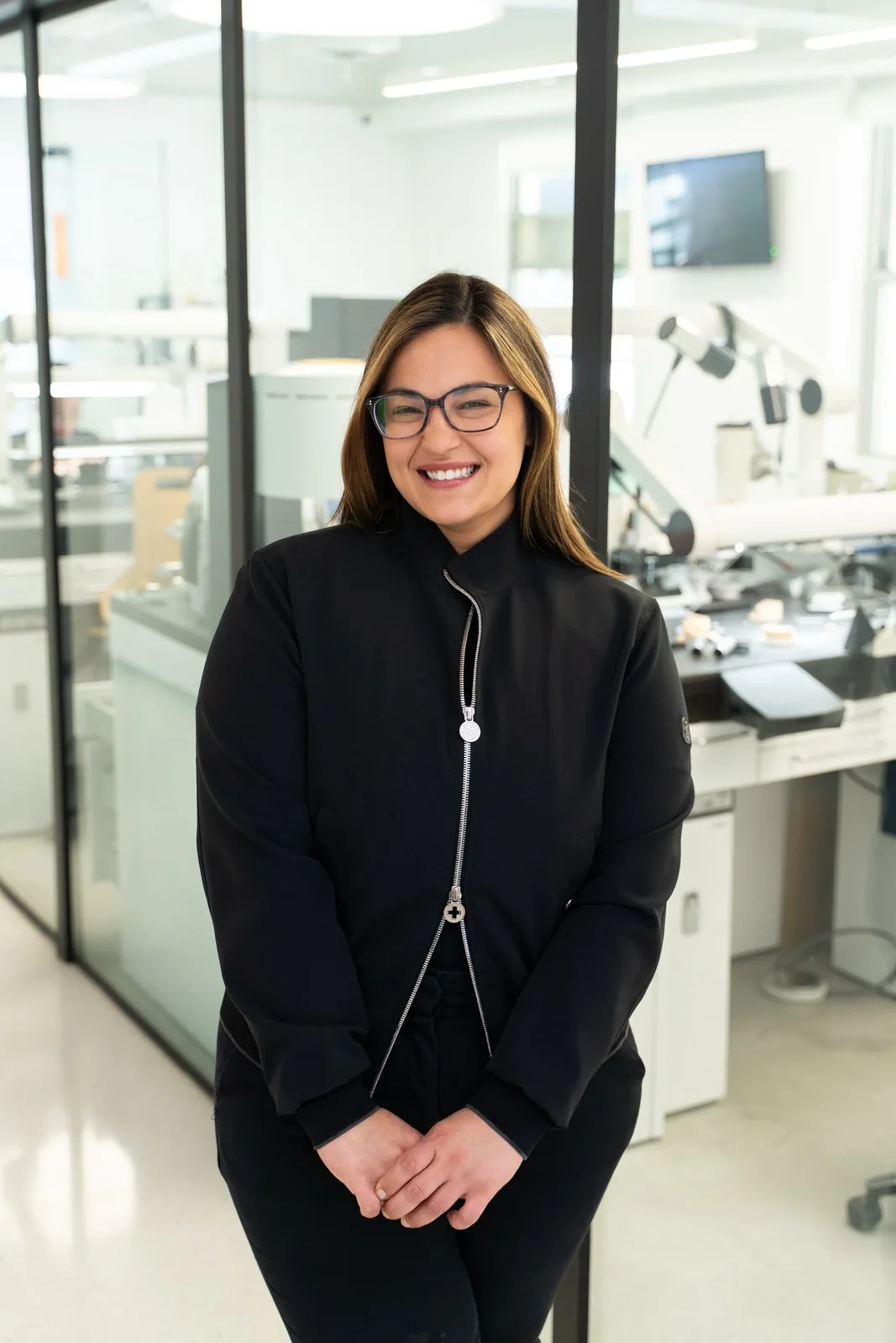 Dr. Andi-Jean Miro in front of the glass-walled dental lab at Apa Aesthetic Los Angeles