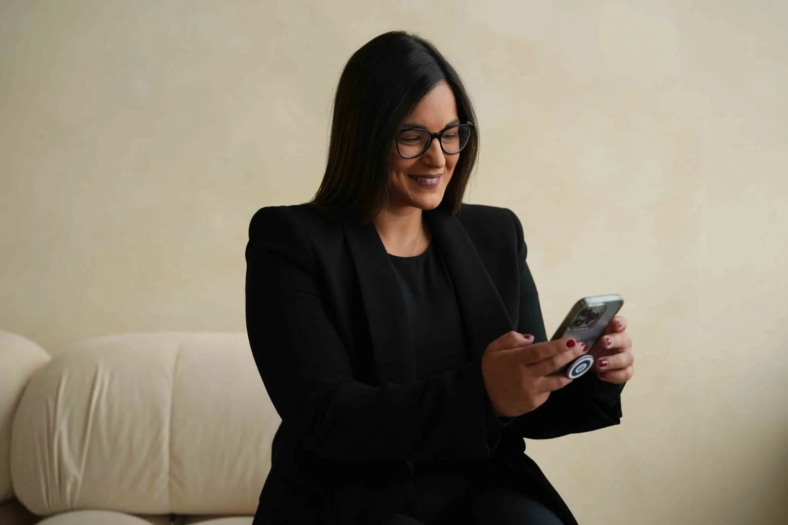 Dr. Andi-Jean Miro seated on a cream sofa, smiling at her phone