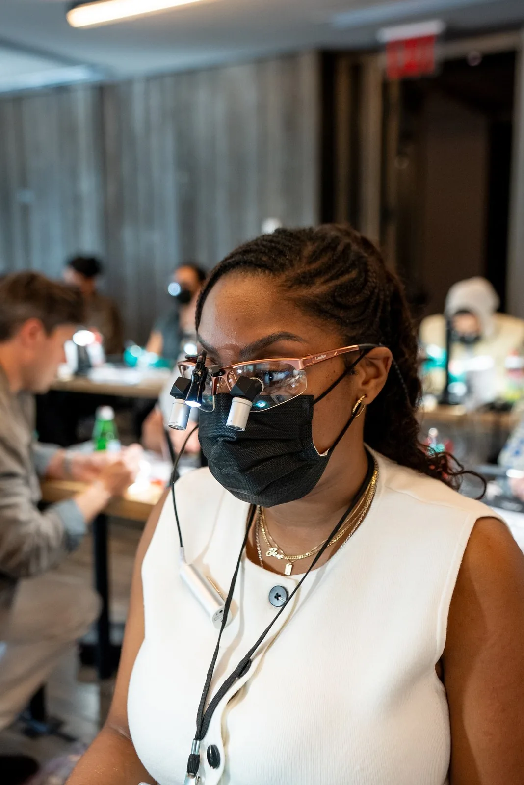 A dentist in lit loupes and a mask concentrates at her workstation