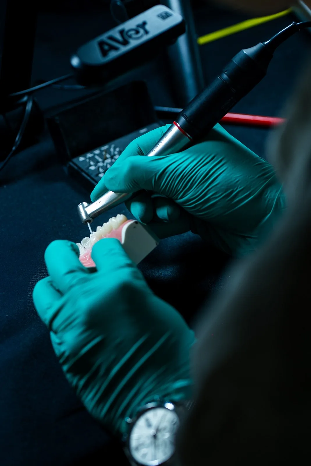Gloved hands prepare a tooth on a typodont with an electric handpiece