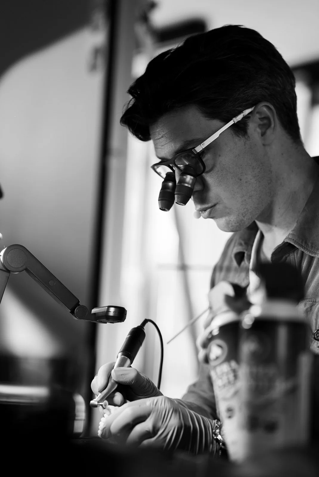 Black-and-white portrait of an instructor in loupes working a model with a handpiece