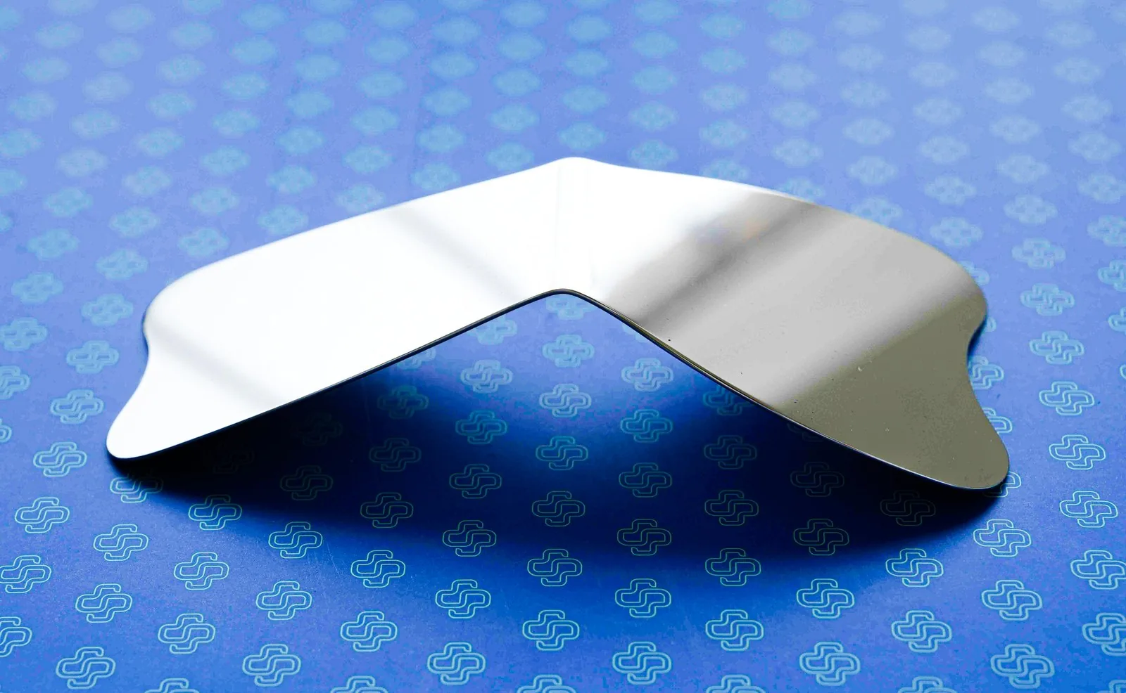 A curved stainless occlusal photography mirror standing on a blue backdrop