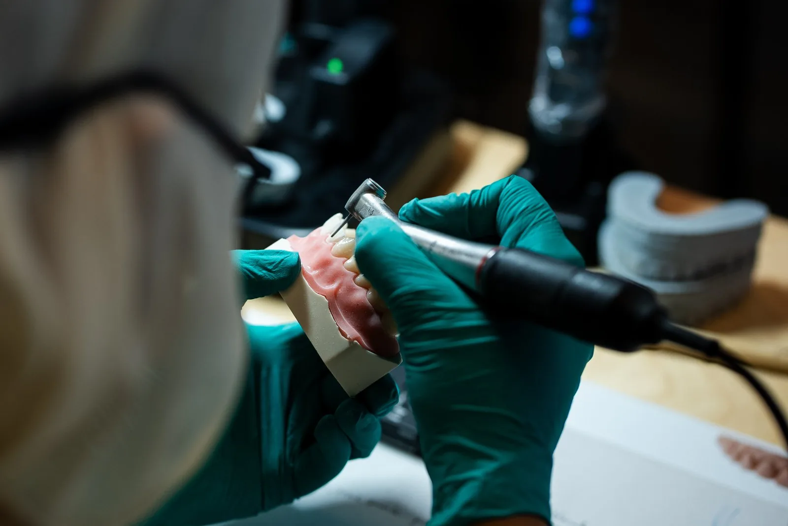 A dentist in teal gloves refines a veneer preparation on a typodont at her bench